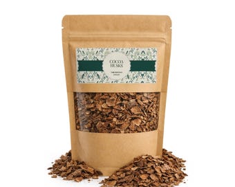 May include: A brown kraft paper stand-up pouch filled with dried cocoa husks. The label features a green botanical pattern, the text COCOA HUSKS, and THEOBROMA CACAO. A pile of loose brown cocoa husks sits in front of the pouch on a white surface.