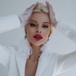 May include: A woman wearing a white blazer with a feather trim collar and white gloves. She has red lipstick and her hair is styled in a bouffant.