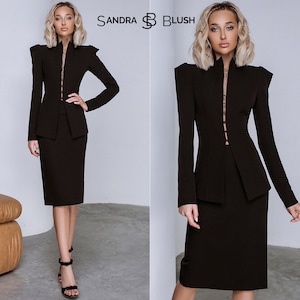 Op de afbeelding: Een zwart tweedelig pak met een jasje met hoge kraag en gestructureerde schouders. De kokerrok komt tot de knie. De merknaam "SANDRA BLUSH" is zichtbaar. Een elegante outfit voor formele gelegenheden.
