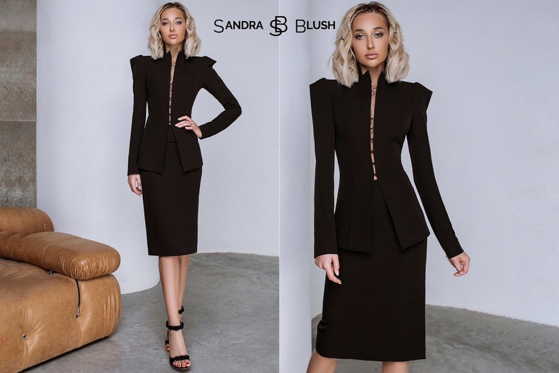Op de afbeelding: Een zwart tweedelig pak met een jasje met hoge kraag en gestructureerde schouders. De kokerrok komt tot de knie. De merknaam "SANDRA BLUSH" is zichtbaar. Een elegante outfit voor formele gelegenheden.