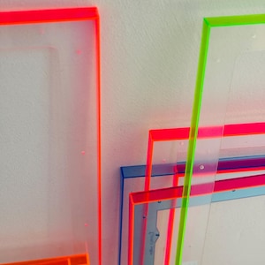 Könnte beinhalten: Eine Ansammlung transparenter, rechteckiger Rahmen mit neonorangen, rosa, blauen und grünen Kanten. Die Rahmen sind geschichtet und überlappen sich, wodurch eine lebendige und moderne Ästhetik entsteht. Die Kanten sind hell gefärbt und kontrastieren mit den klaren Zentren.