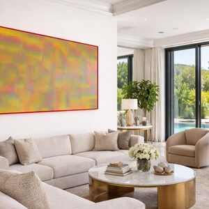 Puede incluir: Un salón moderno con una gran pintura abstracta en tonos amarillos, rosas y verdes, enmarcada en rojo. La habitación cuenta con un sofá seccional, dos sillones y una mesa de centro redonda. Grandes ventanales ofrecen vistas a una piscina y exuberante vegetación.