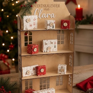 Può includere: Un calendario dell'avvento in legno a forma di casa con la scritta Adventskalender von Clara. Presenta tre ripiani che ospitano piccoli regali avvolti in carta rossa o bianca con motivi di cervi e alberi, ciascuno con un'etichetta numerata in legno.