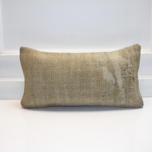 May include: A rectangular beige pillow with a textured surface. The pillow is placed on a white surface and has a faded design on one side. The pillow is a decorative item.