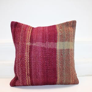 May include: A square decorative pillow with a textured, woven design. The pillow features a color block pattern with shades of burgundy, gold, and tan. The pillow is a square shape and appears to be made of a soft fabric.