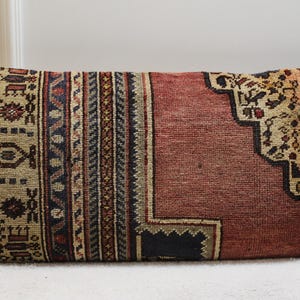 May include: A rectangular pillow with a red, beige, and blue patterned design. The pillow is made of a soft, woven fabric and has a traditional, vintage look.