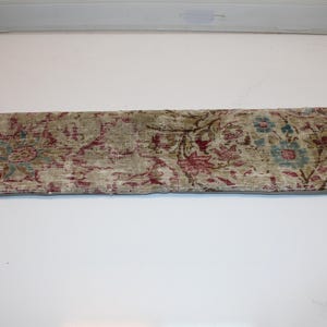 May include: A rectangular, vintage-style pillow with a faded floral pattern in muted tones. The design features burgundy, teal, and olive green against a beige background, creating a distressed, antique look. The pillow is likely for home decor.