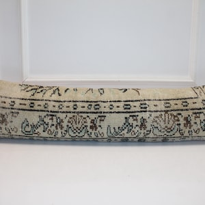 May include: A long, rectangular pillow with a cream-colored background and an intricate, dark brown and tan patterned design. The pillow is placed on a white surface, showcasing its decorative, vintage style.
