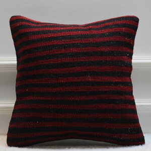 May include: A red and black striped throw pillow made from woven fabric. The pillow is square shaped and has a soft, textured surface.