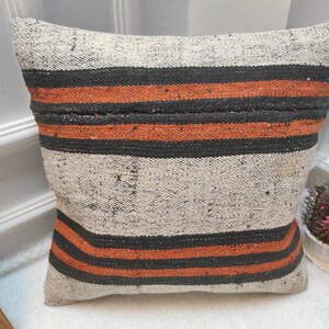 May include: A striped throw pillow with black, orange, and white stripes. The pillow is made of a woven fabric with a textured surface.