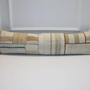 May include: Rectangular decorative pillow with a patchwork design in neutral tones of beige, cream, and brown. A small section features a green zigzag stitch. The pillow is approximately 36 inches long.