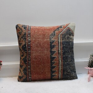 May include: A square throw pillow with a colorful geometric pattern in shades of red, orange, blue, and white. The pillow is made from a woven fabric with a distressed look.