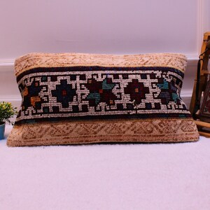 May include: A beige throw pillow with a colorful geometric pattern. The pillow has a dark blue border and a white center with colorful accents.