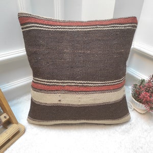 May include: A brown and beige striped throw pillow with red accents. The pillow is made of woven fabric and has a rustic, hand-crafted look.