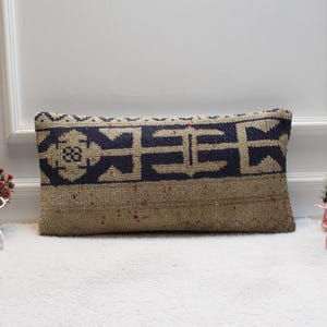 May include: A rectangular throw pillow with a beige background and a blue and white geometric pattern. The pillow is sitting on a white surface.