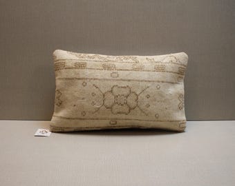 May include: Rectangular beige pillow with a brown floral pattern. The pillow has a woven texture and a faded, vintage appearance. The design features a central floral motif and geometric borders, suggesting a traditional rug design.