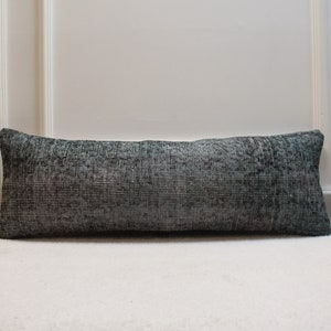 Puede incluir: Una almohada larga y rectangular con un patrón de rayas blancas y negras. La almohada está sobre una superficie blanca.