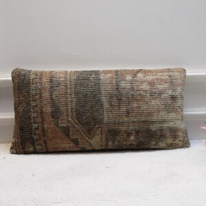 May include: A rectangular pillow with a brown, beige, and pink patterned fabric. The pillow is made from a woven fabric with a distressed look.