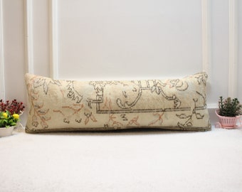 Peut inclure: Un long coussin rectangulaire avec un tissu de couleur crème et un motif floral dans les tons de brun, noir et rose. Le coussin est posé sur une surface blanche.