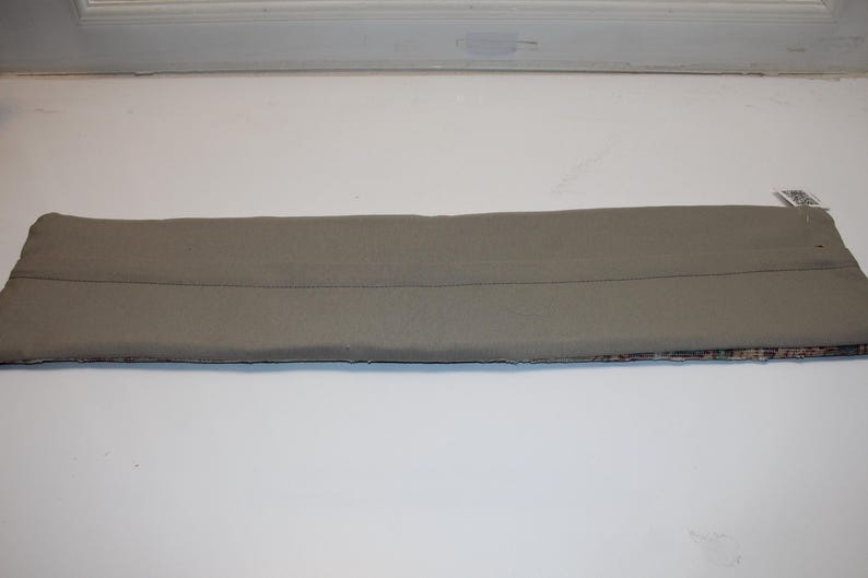 May include: A rectangular, light gray fabric item with a seam down the middle. The bottom edge features a patterned design. The item is likely a car accessory, possibly a sun visor or a similar component.
