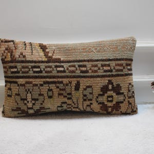 May include: A rectangular pillow with a brown and beige patterned fabric. The pillow has a traditional design with floral motifs and geometric patterns.