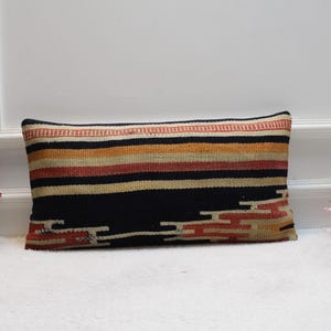 May include: A long rectangular pillow with a black, red, orange, and cream striped pattern. The pillow has a woven texture and is made of a soft, comfortable fabric.