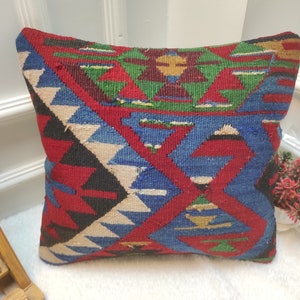 May include: A colourful throw pillow with a geometric pattern in shades of red, blue, green, and white. The pillow is made of woven fabric and has a traditional design.