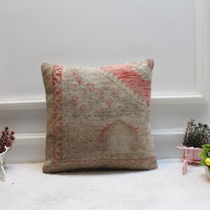 May include: A square throw pillow with a beige background and a red and white geometric pattern. The pillow is sitting on a white fluffy surface.