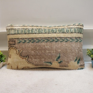 May include: A rectangular pillow with a beige and green patterned design. The pillow is made from a woven fabric and has a fringed edge.