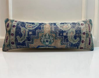 Peut inclure: Coussin rectangulaire décoratif avec un motif de tapis vintage. Le coussin présente un motif central dans les tons de bleu, beige et sarcelle, avec des touches de violet. Les bords ont un aspect délavé et vieilli, ajoutant à son esthétique antique.