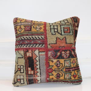 May include: Square decorative pillow with a patchwork design. The pillow features a mix of colors including red, yellow, and beige, with geometric and floral patterns. The pillow is likely made of a woven fabric.
