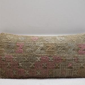 May include: A long rectangular pillow with a woven pattern in shades of beige, brown, and pink. The pillow has a traditional, ethnic design.
