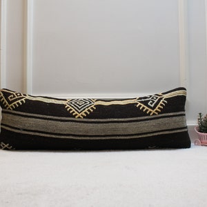 Puede incluir: Una almohada larga de color negro y blanco con un diseño geométrico. La almohada está sobre una superficie blanca.