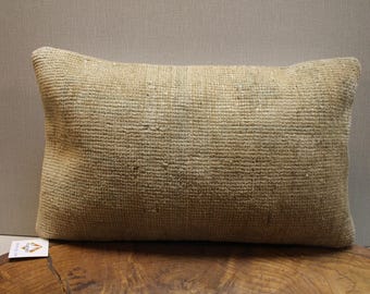 May include: A rectangular beige pillow with a textured, woven surface. The pillow is placed on a wooden surface and has a neutral background. The pillow is a decorative item, likely for a living room or bedroom.