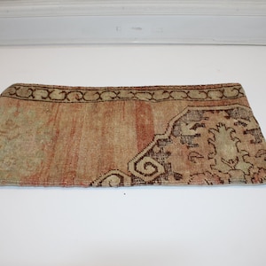 May include: A rectangular pillow cover featuring a faded, woven textile pattern in shades of muted orange, beige, and dark brown. The design includes a decorative border with a repeating scroll motif and a central area with intricate floral elements.
