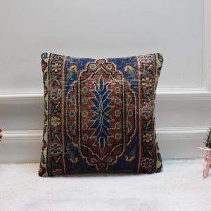May include: A square throw pillow with a blue, red, and green patterned design. The pattern is intricate and features a floral motif. The pillow is made of a soft, woven fabric.