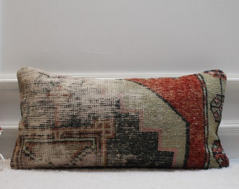May include: A rectangular cushion with a colourful, geometric pattern in shades of red, green, black, and white. The cushion is made from a woven fabric with a distressed look.