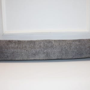 May include: A long, rectangular gray pillow with a textured surface. The pillow is made of a woven material and is placed horizontally. The pillow is approximately 36 inches long.