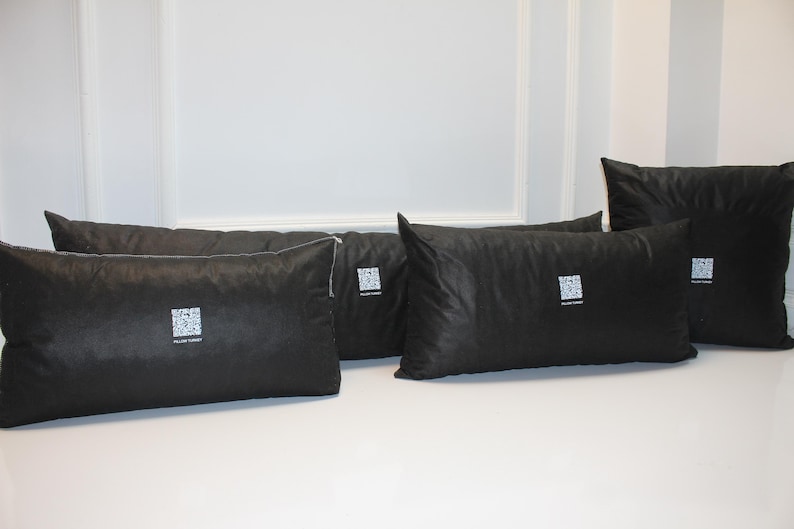 May include: Several black pillows of varying sizes are arranged on a white surface. Each pillow has a square, white graphic and text. The pillows are rectangular and square, with a smooth, dark fabric.