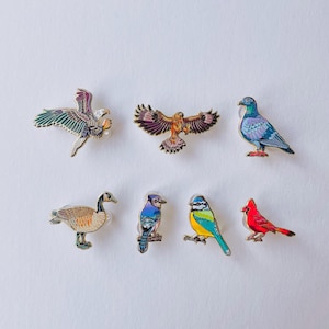 a collection of six bird pins, each with a unique design and color, arranged in a grid pattern on a white background.