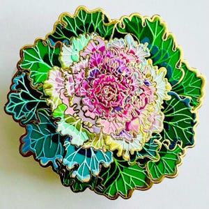 a vibrant, intricately designed flower with a variety of colors, including pink, green, and white. The flower is surrounded by a lush, green leafy background, creating a visually striking and detailed composition.