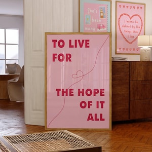 以下が含まれることがあります： 「TO LIVE FOR THE HOPE OF IT ALL」の赤い文字が入った、額入りのピンク色のアートプリント。他に2つの額入りのプリントがあり、1つは「She's been many」という文字、もう1つはハートのデザインと文字が入っています。