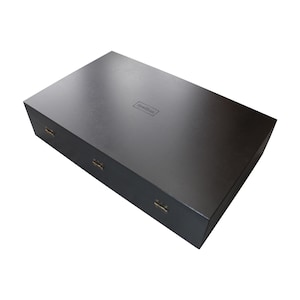 May include: A rectangular dark brown wooden box with a smooth finish and a hinged lid. The top of the box features the word Spellbinders embossed in the center. Three small metal hinges are visible along the front edge of the box.