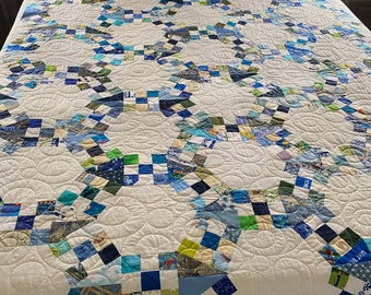 May include: A white quilt with a blue and green patchwork design. The quilt is made up of small squares of fabric sewn together in a pattern. The quilt is quilted with a white thread and has a white backing.