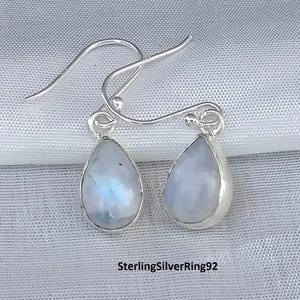 May include: A pair of silver dangle earrings with teardrop-shaped moonstone gemstones.