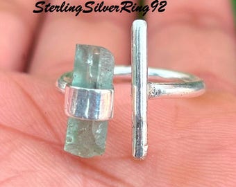 Könnte beinhalten: Ein Silberring mit einem rohen, hellblau-grünen Aquamarin-Kristall und einem vertikalen Silberstab. Der Ring hat ein schlichtes, modernes Design. Der Text "Sterling Silver Ring 92" ist sichtbar.