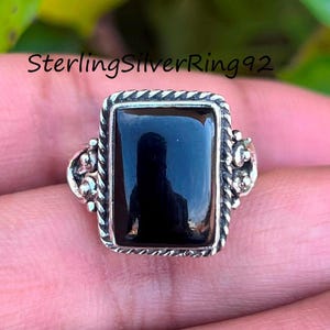 Peut inclure: Une bague en argent avec une pierre rectangulaire noire. La bague a un design détaillé autour de la pierre.