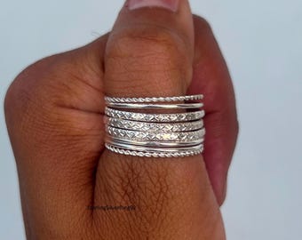 May include: A collection of silver rings with various textures, including twisted rope and diamond patterns. The rings are stacked on a finger, showcasing the different designs and the overall shine of the metal. The rings are a jewelry item.