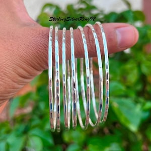 May include: A set of seven silver hammered bangle bracelets. The bracelets are stacked on top of each other and are all the same size.