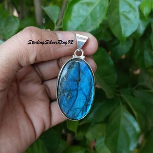 May include: A silver pendant with a large oval blue labradorite gemstone. The pendant has a silver bail for attaching to a chain.